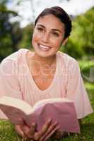 Woman looks upwards while reading a book as she is lying down