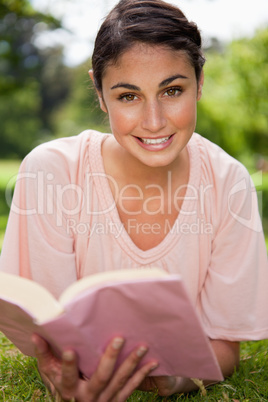 Woman looking ahead while reading a book as she is lying down