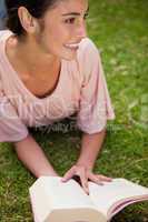 Woman looks to the side while reading a book as she is lying dow