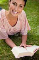 Smiling woman looking up while reading a book as she lies down