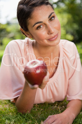 Woman offers an apple while lying in grass
