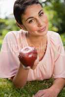 Woman offers an apple while lying in grass