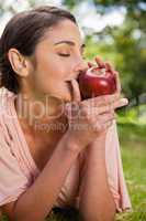 Woman smells an apple while lying in grass