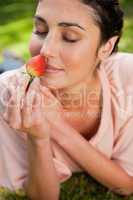 Woman smells an strawberry while lying in grass