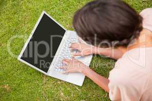 Woman using a laptop while lying in grass