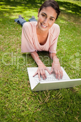 Woman looking ahead while using a laptop as she lies down in gra
