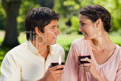 Two friends smiling towards each other while holding glasses of