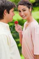 Woman looks to the side while offering a strawberry to her frien