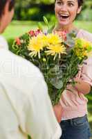 Woman surprised as she is presented with flowers by her friend