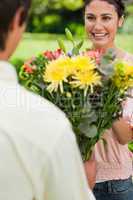 Woman smiling as she is presented with flowers by her friend