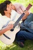 Man playing the guitar while his friend leans on his shoulder