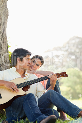 Man looking down while playing the guitar as his friend watches