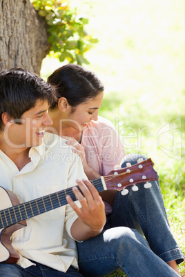 Woman laughing with her friend who is playing the guitar