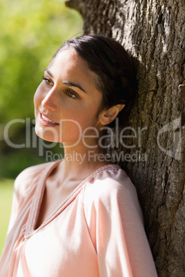 Woman looking into the distance while sitting against a tree