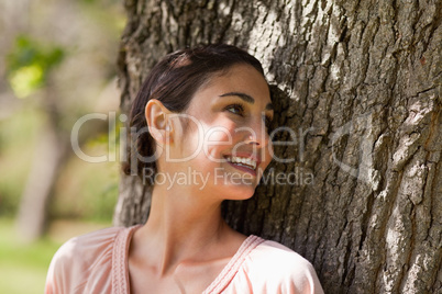 Woman looking over her shoulder while sitting against a tree