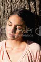 Woman closing her eyes while sitting against a tree