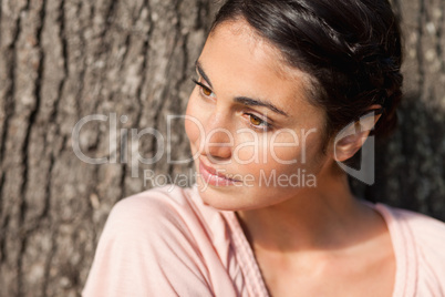 Woman looking to her side while sitting by a tree with the sun s