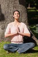 Woman sitting in a yoga pose with her hands joined near a tree