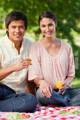 Woman and her friend smiling while holding glasses of juice duri