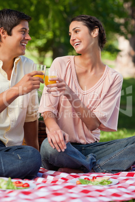 Woman laughing as she touches glasses of juice with her friend d