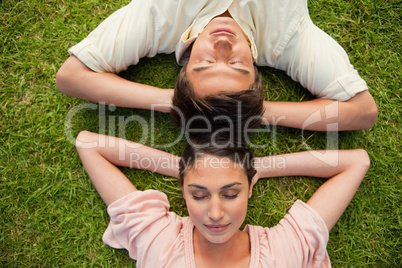 Close-up of two friends lying head to head with both hands behin