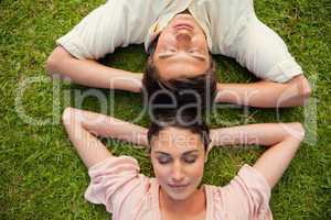 Close-up of two friends lying head to head with both hands behin