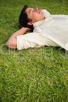 Man lying in grass with his eyes closed and both hands behind hi