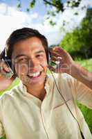 Man smiling while using headphones to listen to music in a park