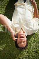 Man laughing while using a phone as he lies on the grass
