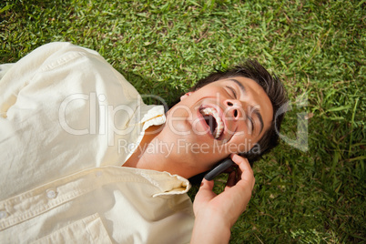 Man laughing while making a call while using a phone as he lies