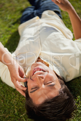 Close-up of a man laughing while using a phone as he lies on the