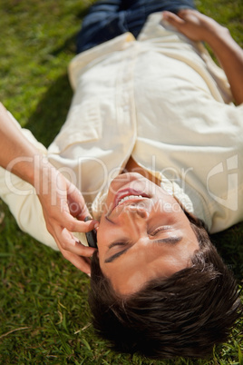 Close-up of a man making a call while using a phone as he lies o