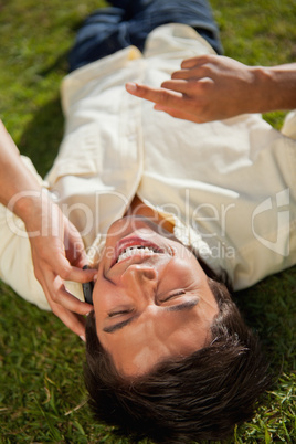 Man with his hand raised laughing while using a phone as he lies