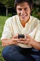 Man smiling while writing a text message as he is sitting down