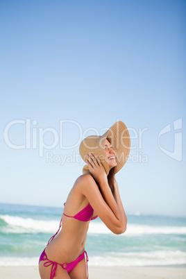 Young woman laughing while standing on the beach and holding her