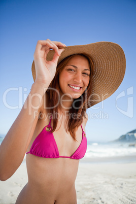 Young smiling woman holding her hat brim while wearing a pink sw
