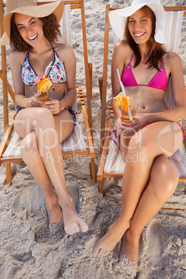 Young women laughing in deck chairs while holding fruit cocktail
