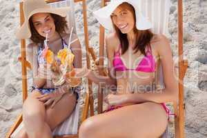 Young women in beachwear clinking their cocktails while looking