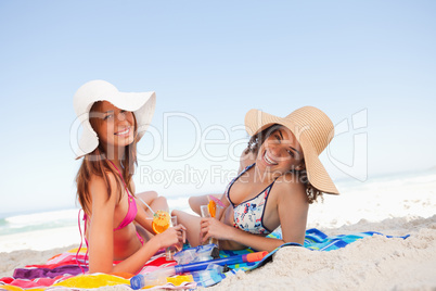 Young smiling women lying on beach towels while looking at the c
