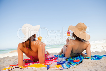 Back view of beautiful women sunbathing while sipping cocktails