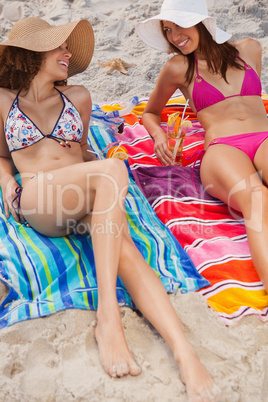 Young women lying on beach towels with cocktails while looking a