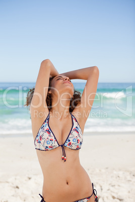 Young woman in bikini raising her arms and looking up