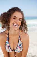 Young woman laughing while standing on the beach and leaning her