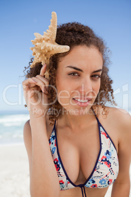 Young attractive woman holding a starfish next to her head