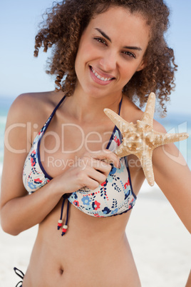 Young attractive woman holding a starfish in front of her should