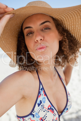 Young woman puckering her lips while holding her hat brim