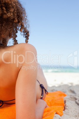 Back view of a young woman lying on her orange beach towel