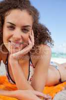 Young pretty woman lying on the beach with her hand on her cheek