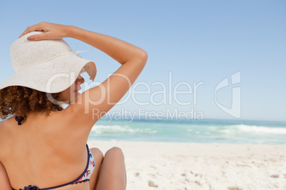 Young woman sitting on a beach towel while holding her hat