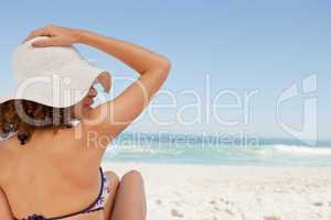 Young woman sitting on a beach towel while holding her hat